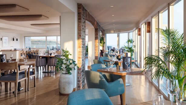 En rummelig restaurant med højt til loftet, store vinduer og en blanding af mursten og træ.