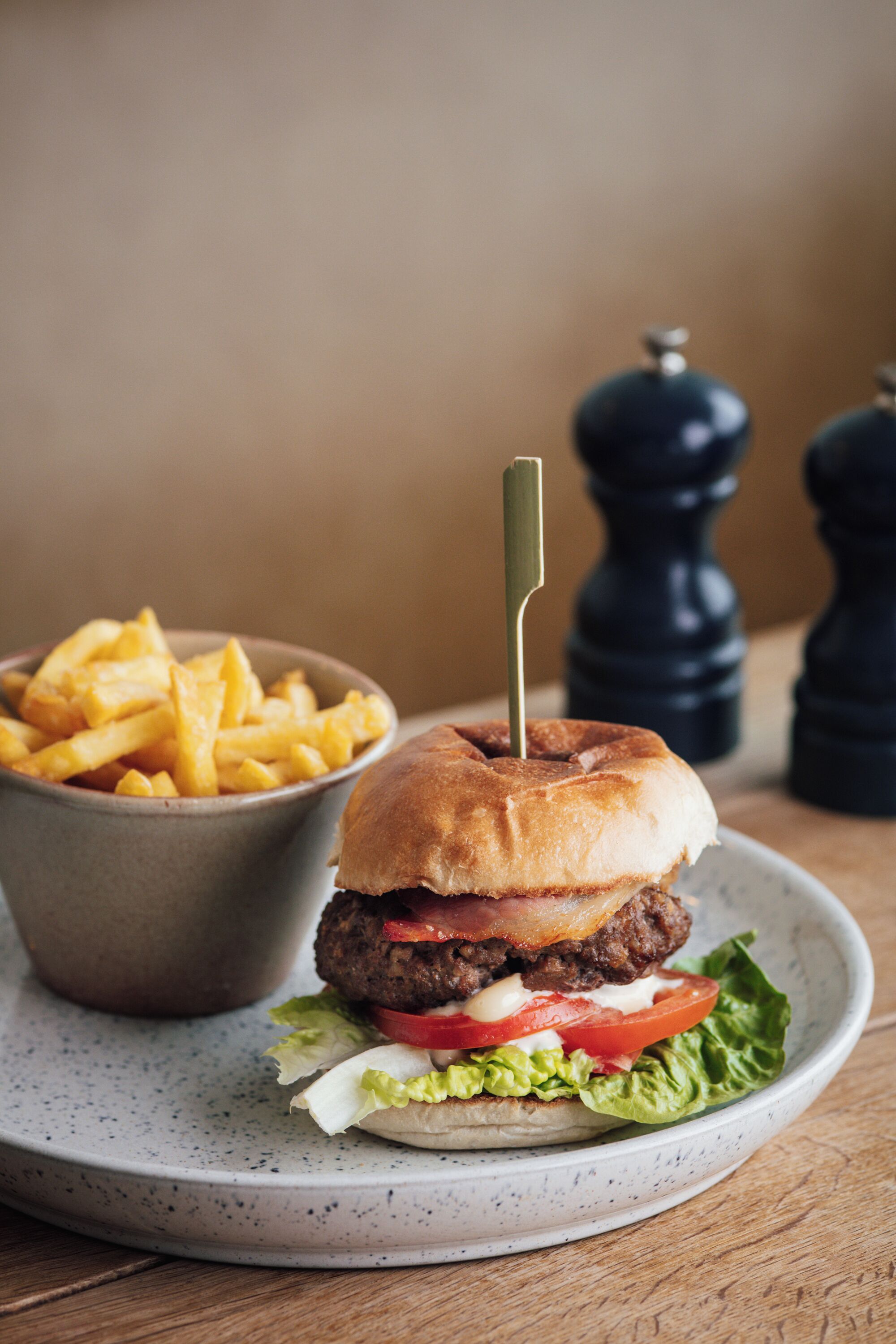 A burger with a toothpick, lettuce, tomato, and a bun, served with French fries on a speckled plate.