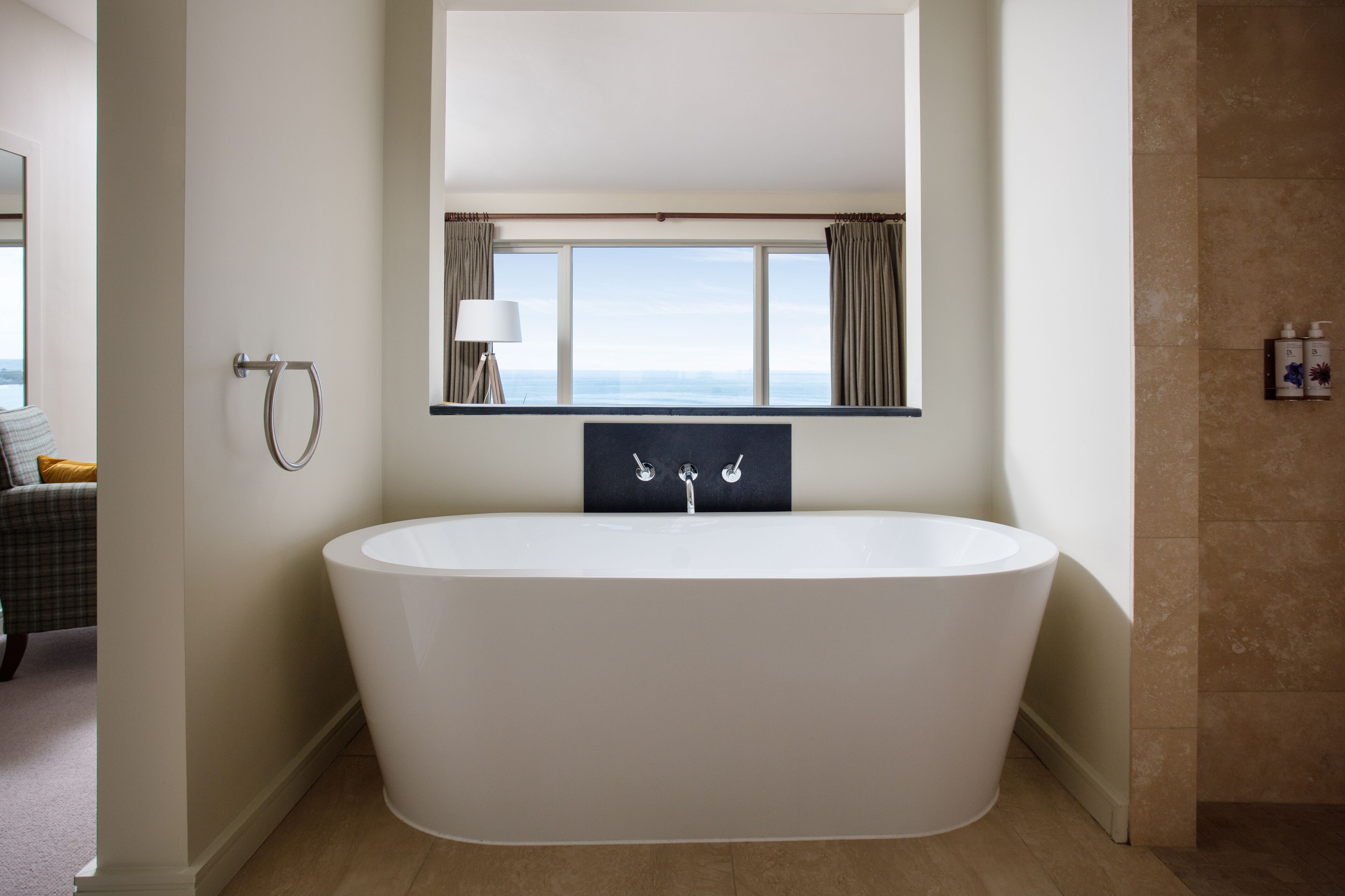 A modern bathroom with a freestanding bathtub, a large mirror, and a view of the sea.