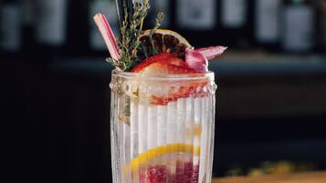 A clear glass with a straw, garnished with a sprig of rosemary, a slice of orange, and a strawberry.