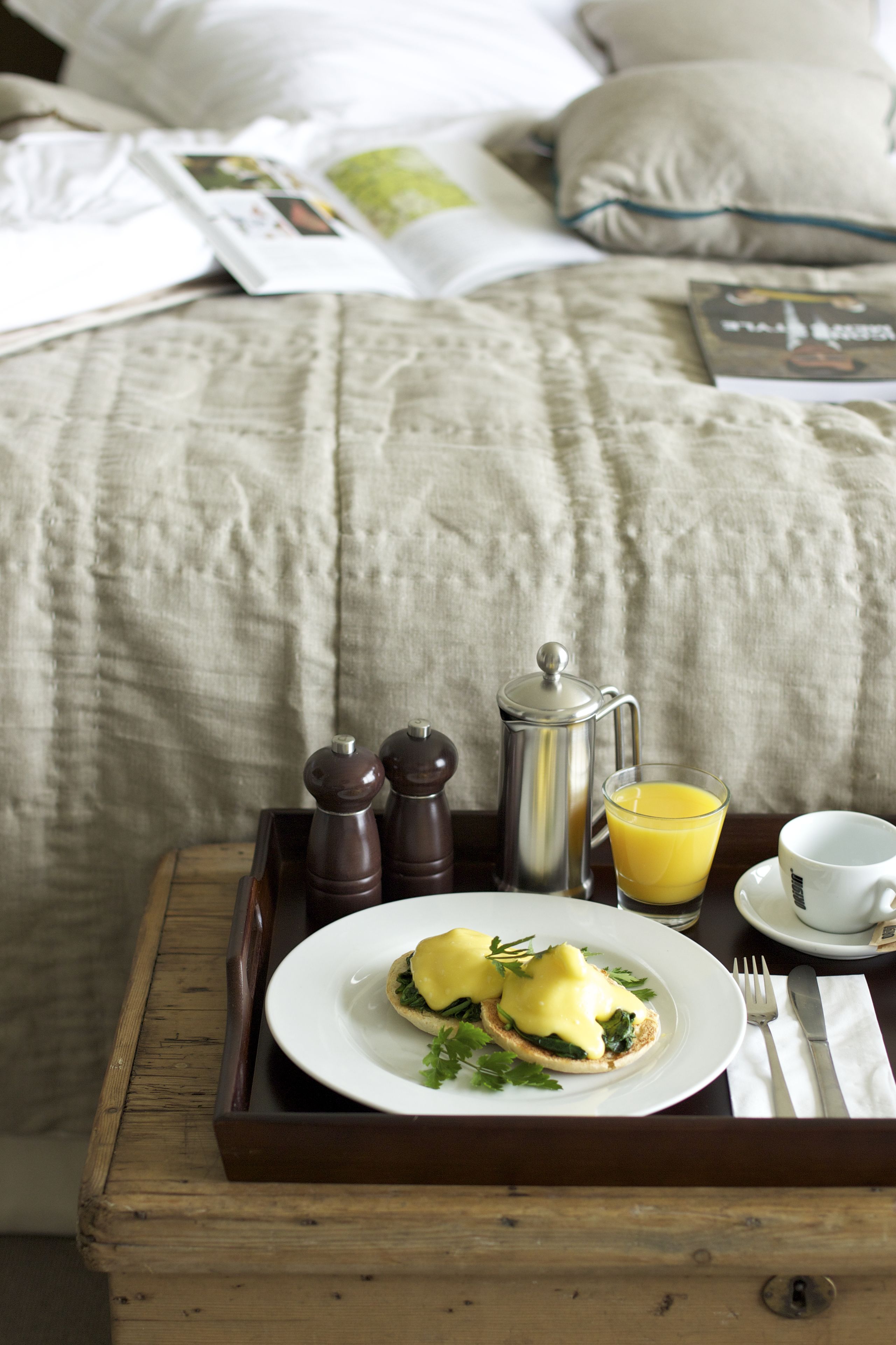 Ein Frühstücksbrett mit Eggs Benedict, Kaffee und Saft auf einem Holztisch in einem Hotelzimmer.