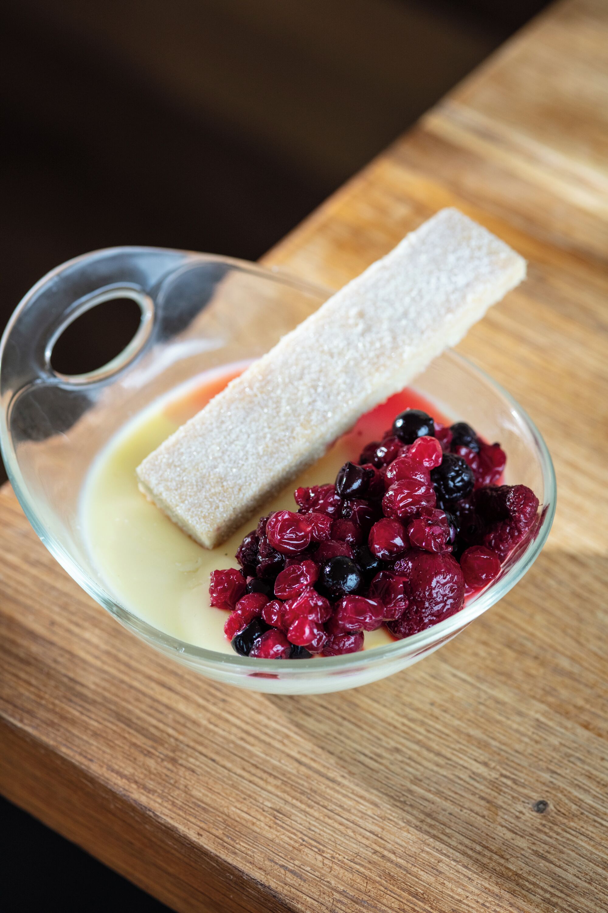 A dessert with a piece of cake and berries in a glass bowl on a wooden table.