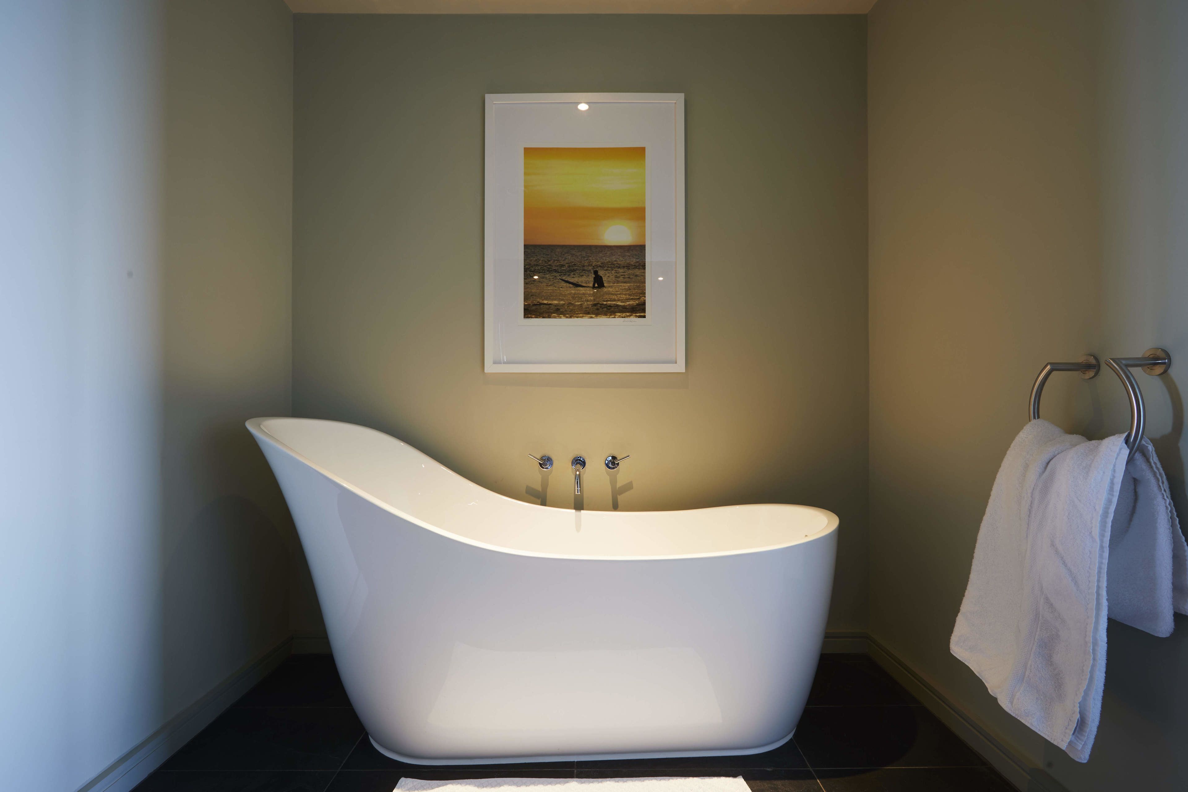 A modern bathroom with a freestanding bathtub, a framed picture on the wall, and a towel rack with a towel.