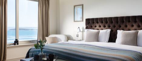 A bedroom with a large bed, a view of the ocean, and a wooden nightstand with a tray.