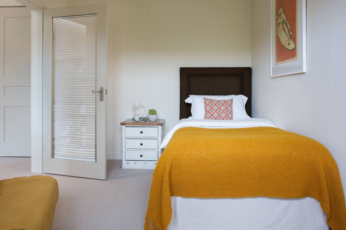 A bedroom with a bed, a nightstand, a chair, a door, and a wall with a framed picture.