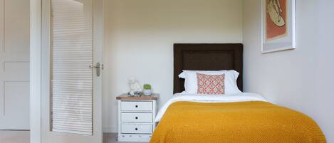 A bedroom with a bed, a nightstand, a chair, a door, and a wall with a framed picture.