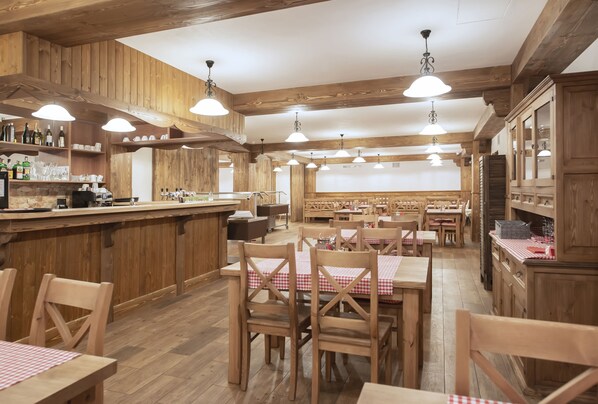 L’intérieur d’un restaurant, avec des meubles en bois, des tables recouvertes de nappes à carreaux et des lampes suspendues.