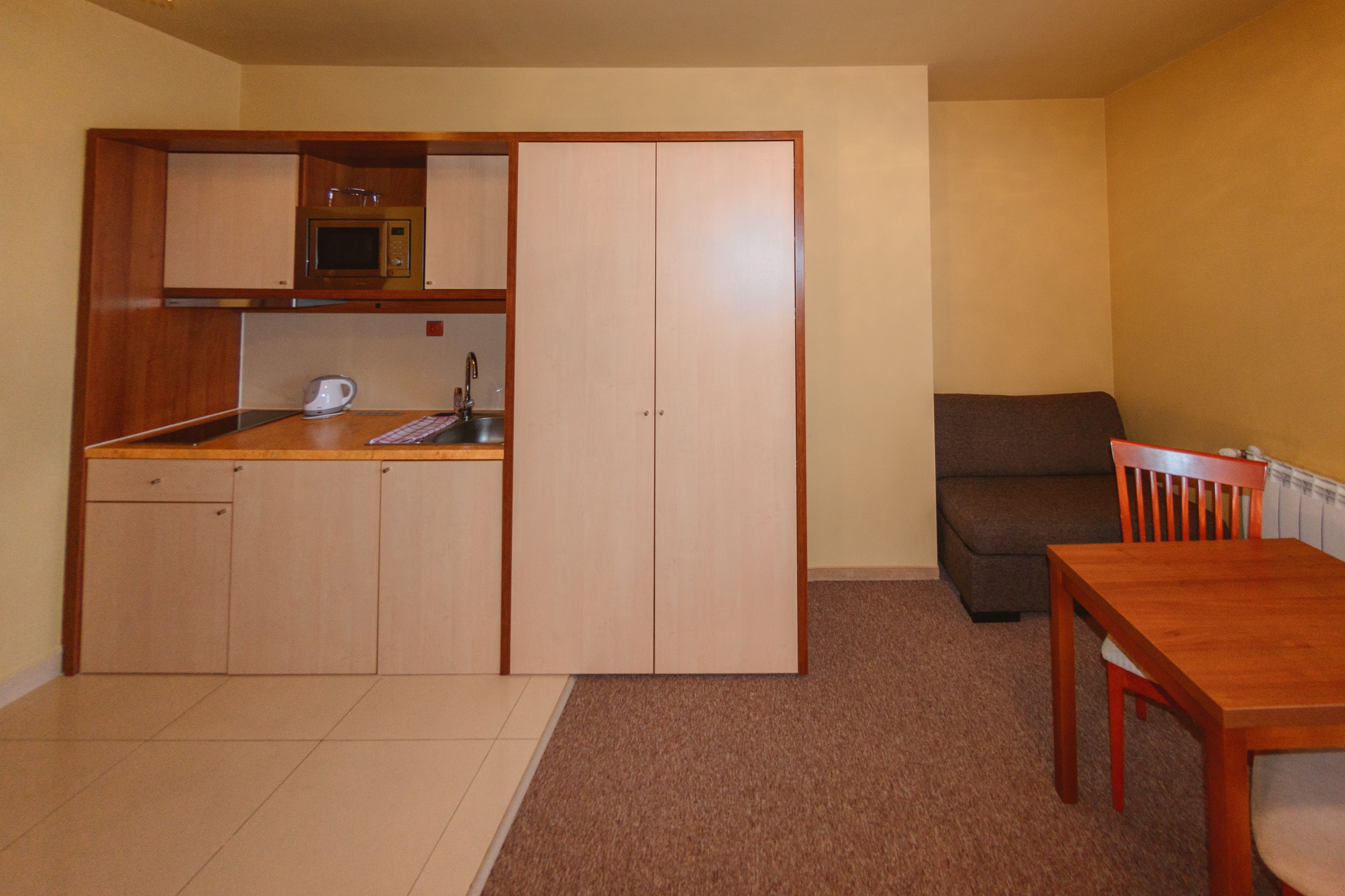 A compact kitchen with a microwave, kettle, and a small sink. There is a dining table with chairs and a sofa in the living area.