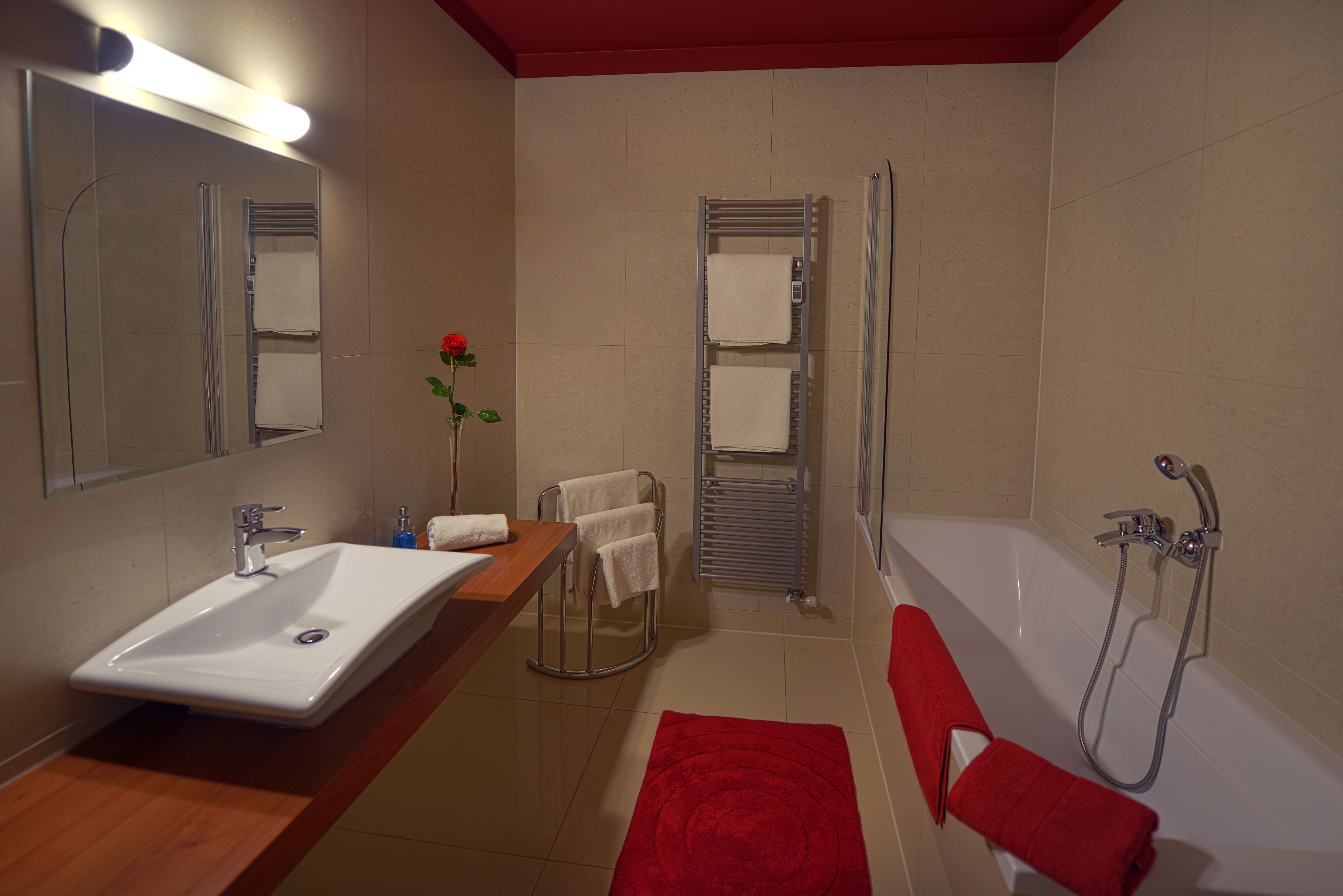 Un bagno moderno con lavandino, specchio, doccia e asciugamani rossi.