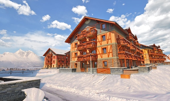Un gran lodge de varios pisos con un telesilla, rodeado de nieve y montañas.
