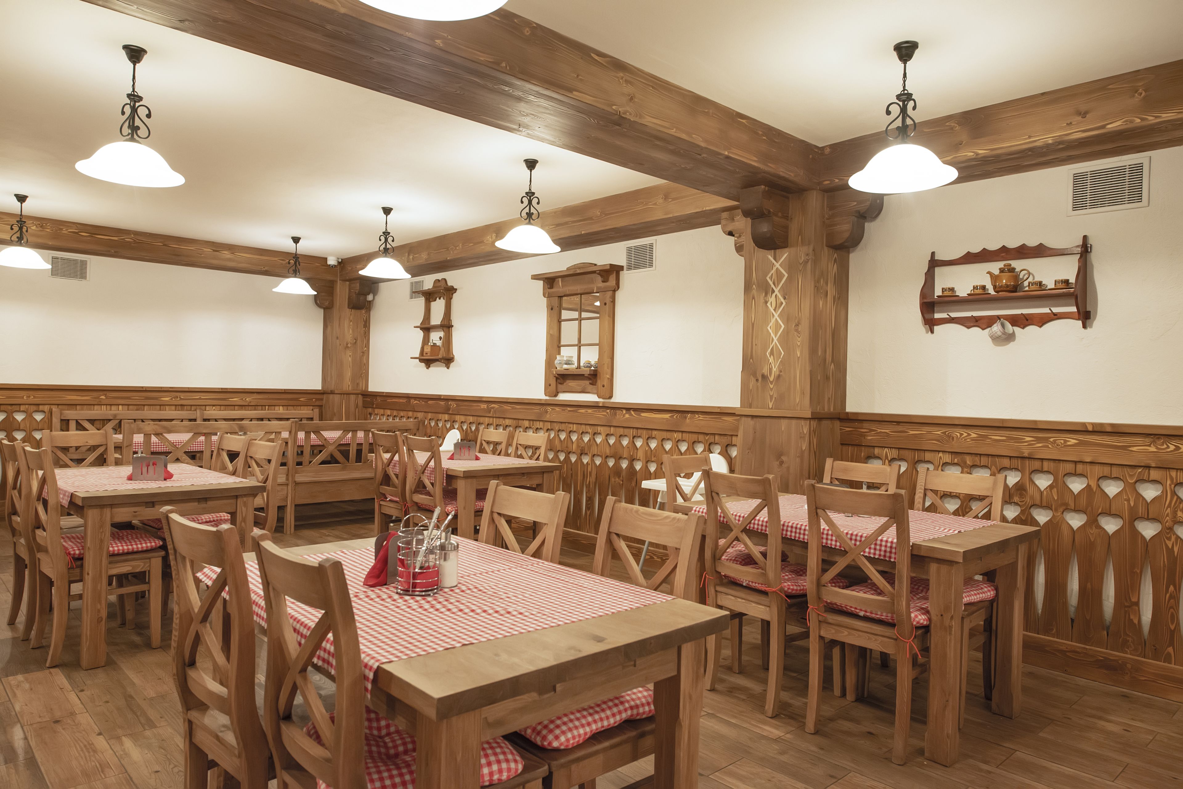 A restaurant with wooden tables and chairs, white walls, and wooden beams on the ceiling.