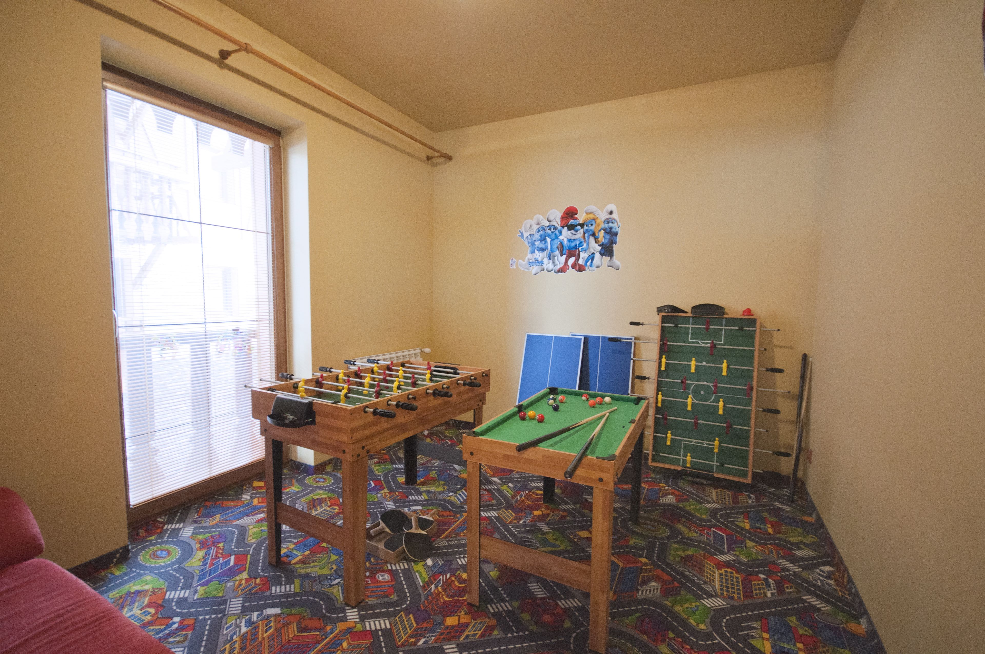 A room with a foosball table, a pool table, and a colorful carpet.