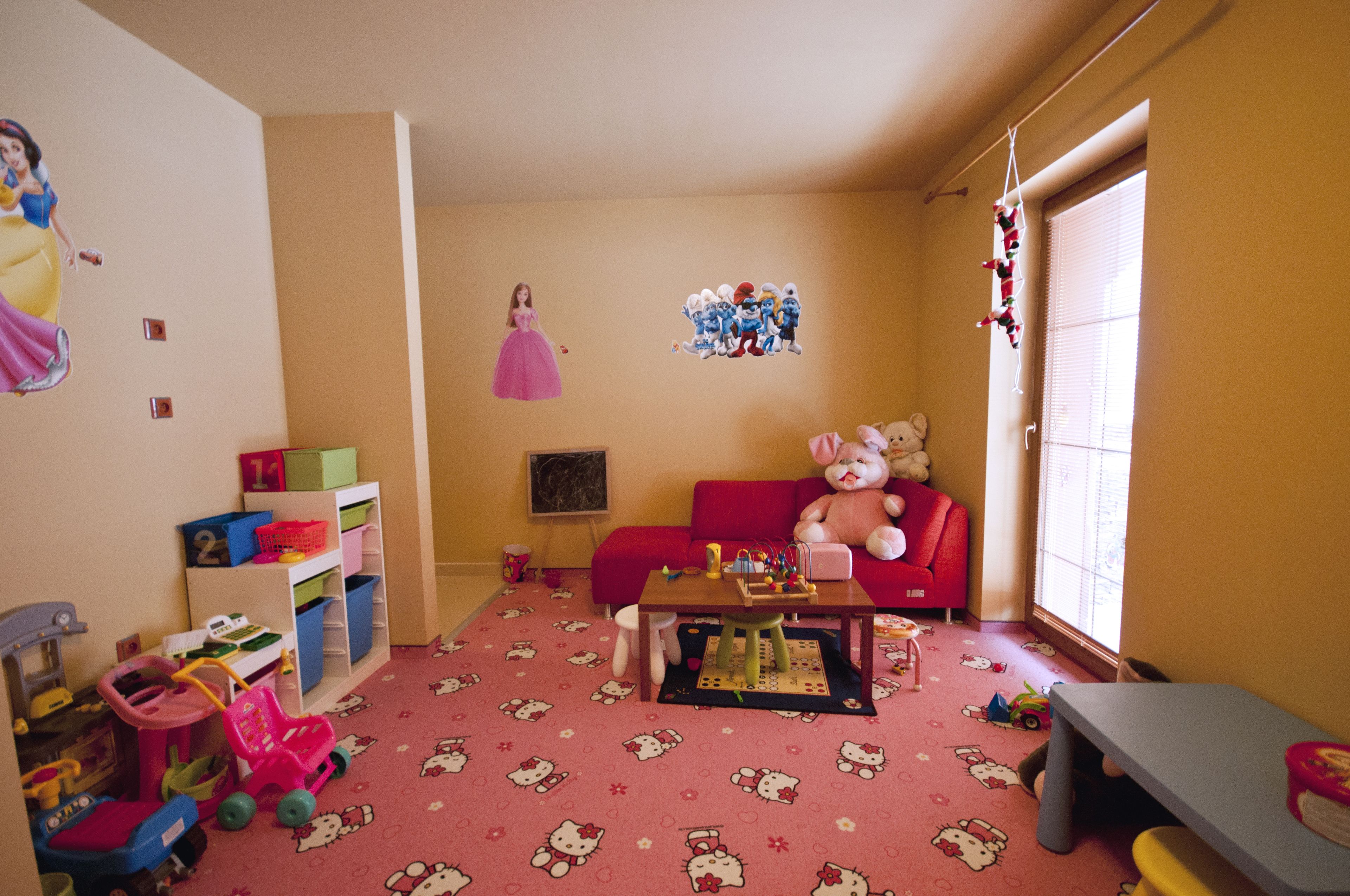 A child's playroom with a pink carpet, a red sofa, and various toys.