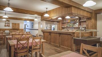 A restaurant interior with wooden tables and chairs, a bar area, and a kitchen visible in the background.