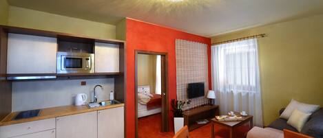 Una habitación de hotel compacta con kitchenette, comedor, sofá y televisor.