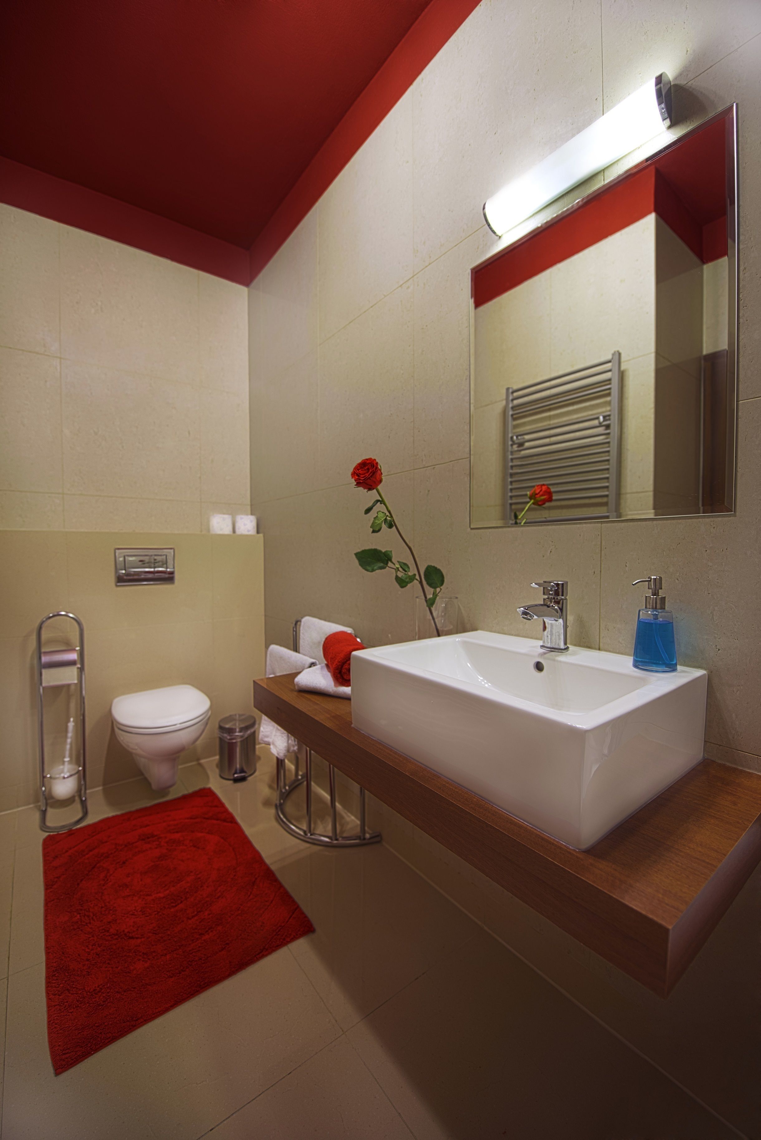 A modern bathroom with a white sink, red accents, a mirror, and a red rose.