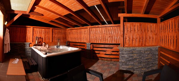 A hot tub in a wooden cabin with a stone wall and wooden benches.