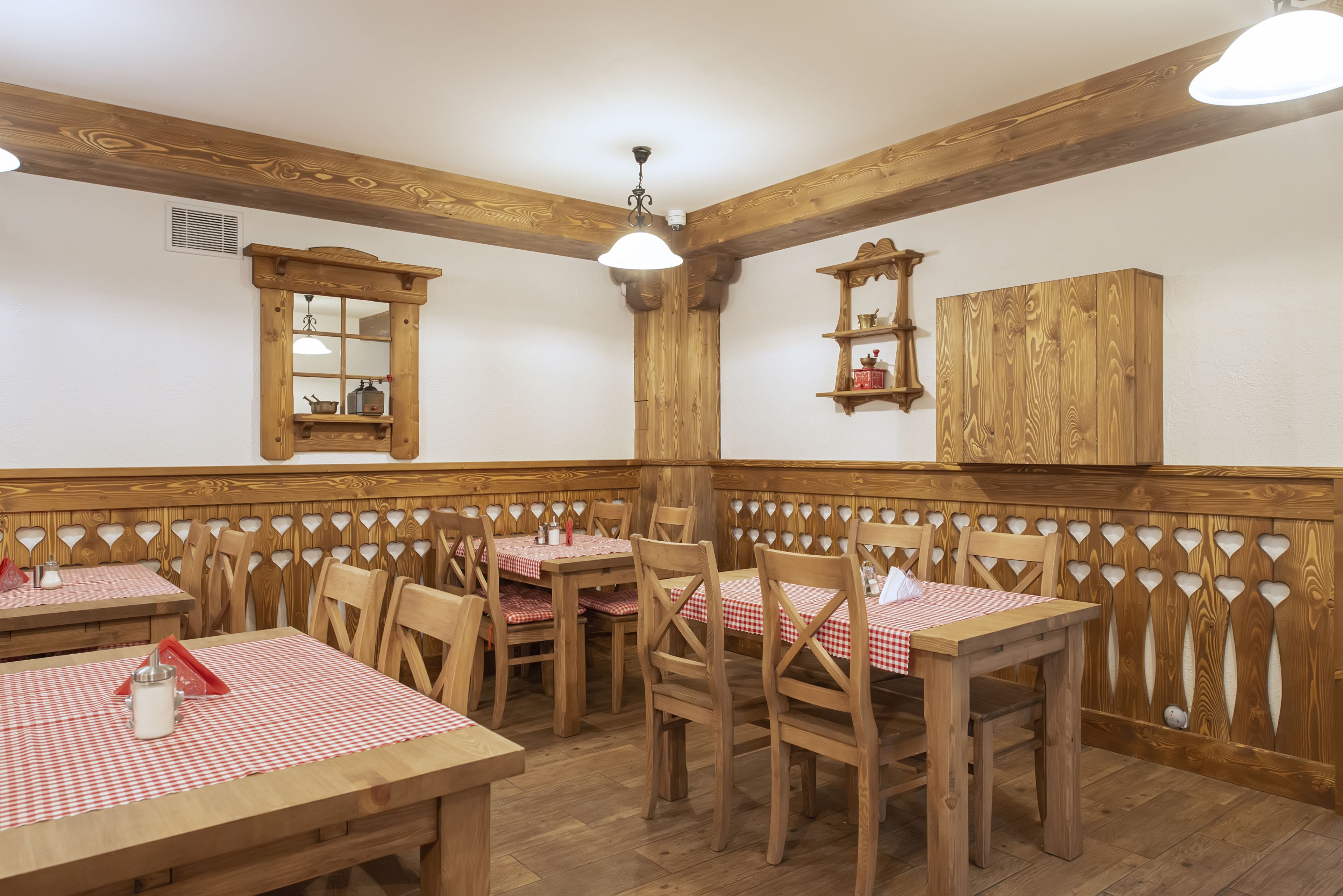 A restaurant with wooden furniture, checkered tablecloths, and a wooden partition wall.