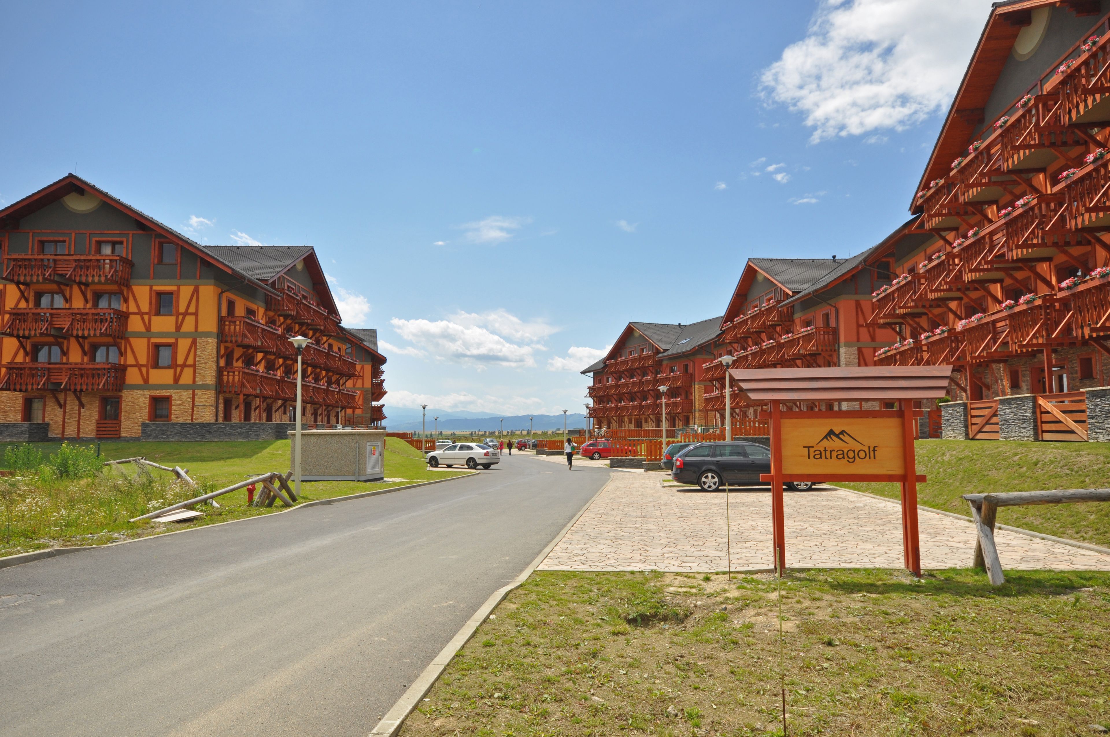 A row of traditional wooden buildings with balconies, a paved road, and a sign reading "Tatragolf."