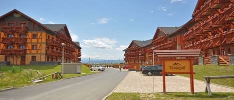 A row of traditional wooden buildings with balconies, a paved road, and a sign reading "Tatragolf."