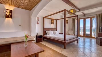 Una habitación con cama con dosel, un banco de madera, una mesita con un florero y vistas al exterior a través de amplias ventanas.