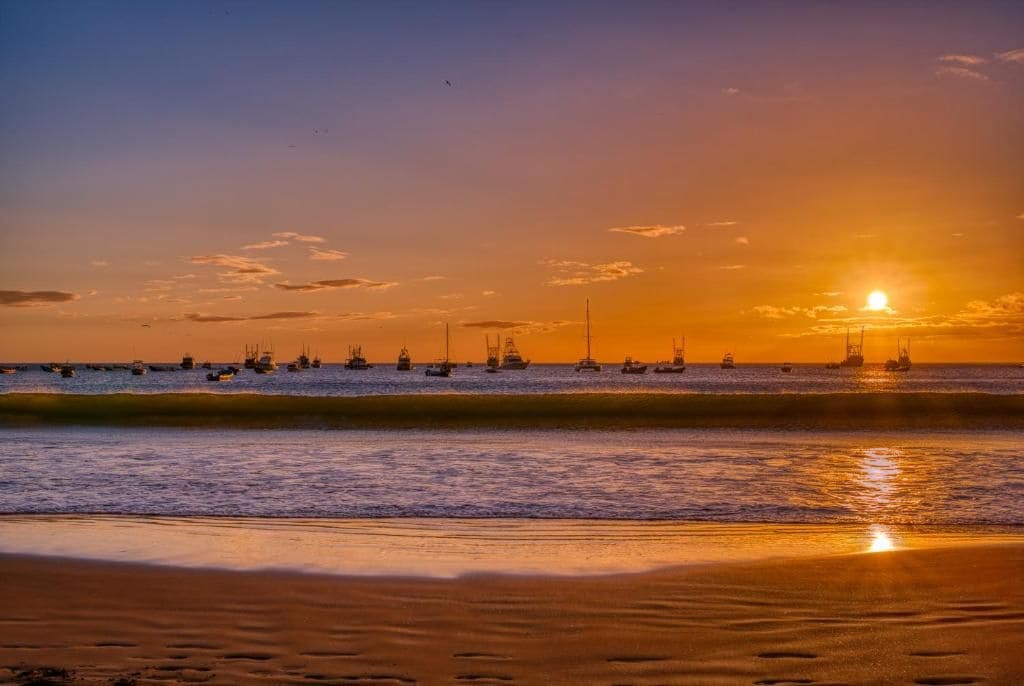 Una playa al atardecer con barcos en el agua.