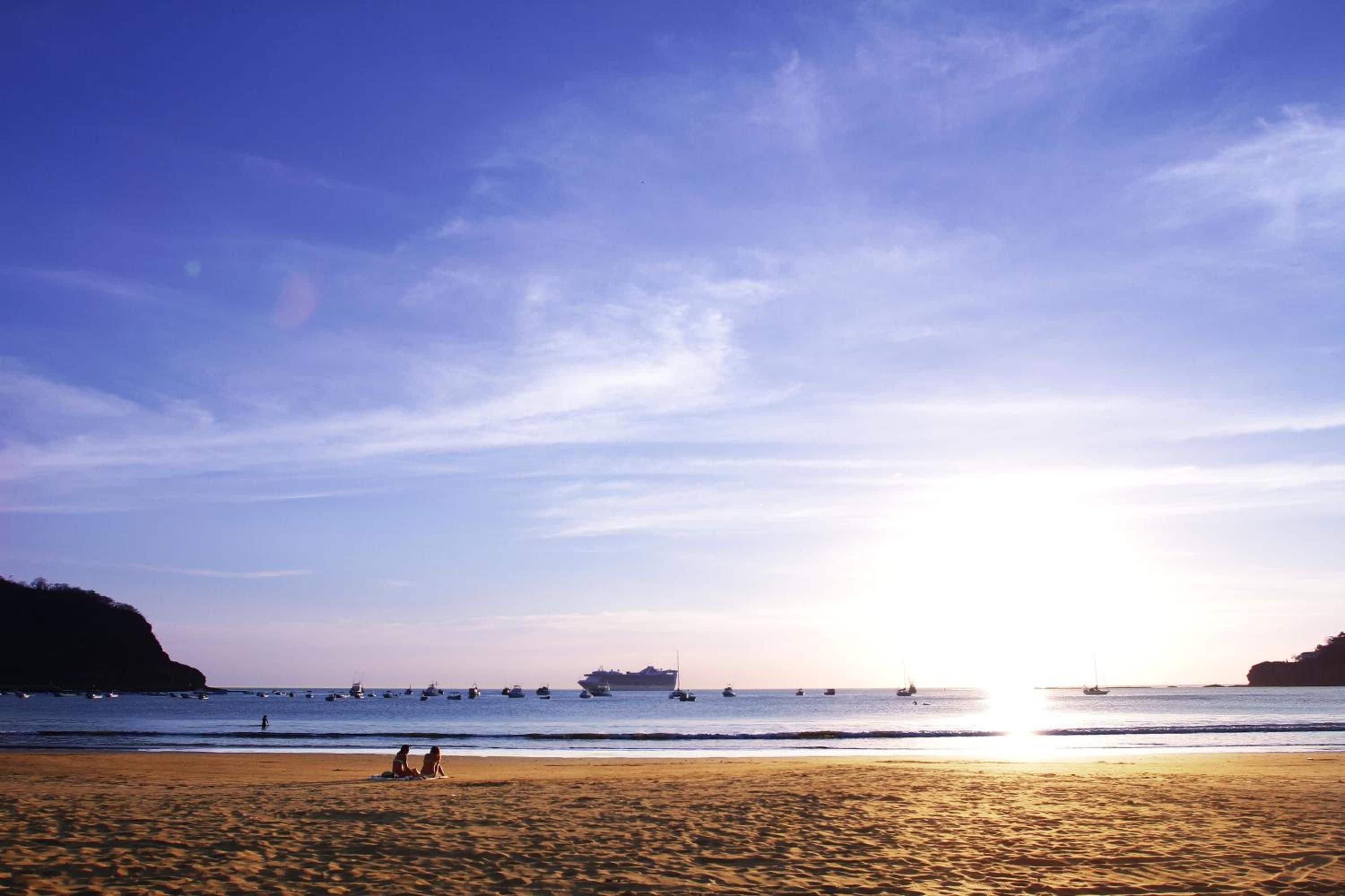 Una platja amb un capvespre, mar tranquil·la i embarcacions.