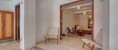 Un hall d’entrée spacieux, doté d’un sol carrelé, d’une porte en bois et d’un coin salon avec une chaise et une petite table.