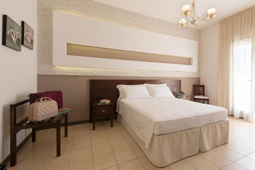 A hotel room with a large bed, a nightstand, a chair, a small table, and a wall-mounted TV.