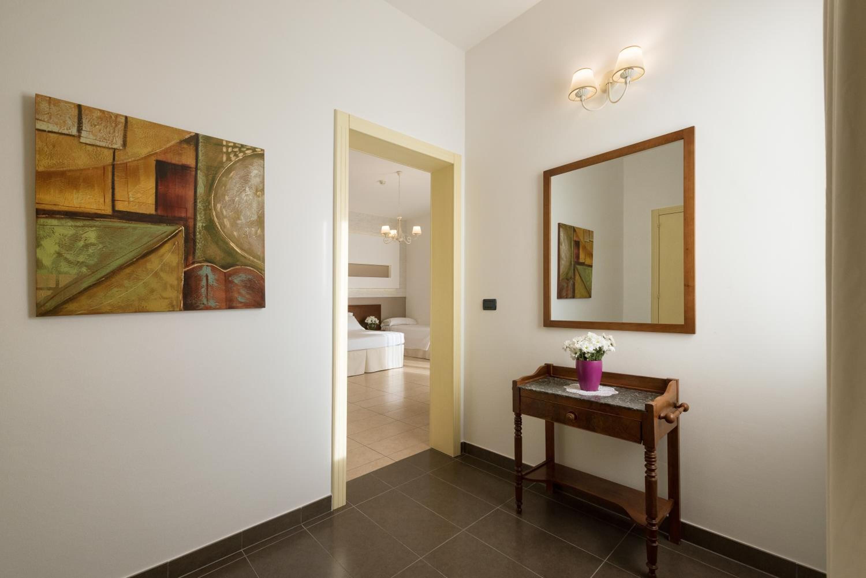A hallway with a painting, a mirror, and a small table with a vase.