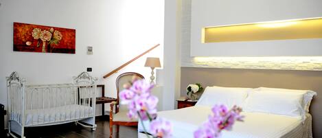 A bedroom with a bed, a crib, a chair, and a nightstand with a lamp.