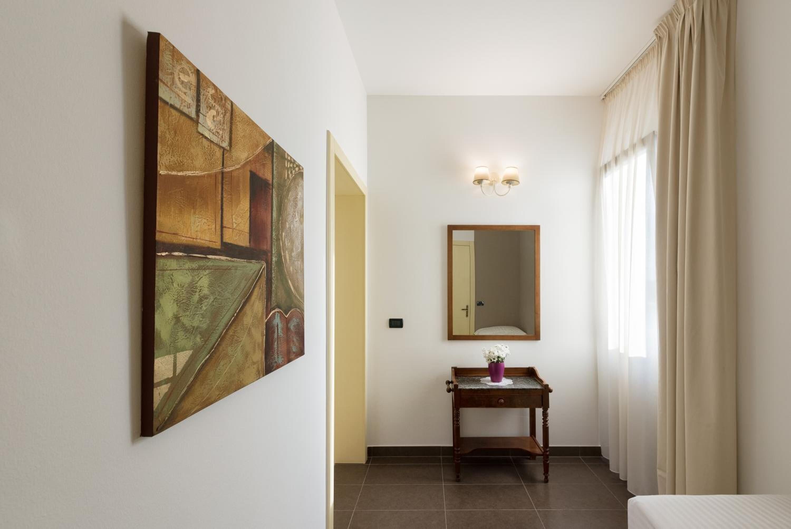 Habitación de hotel con un cuadro abstracto grande, un espejo, una mesita con un jarrón y una cama.