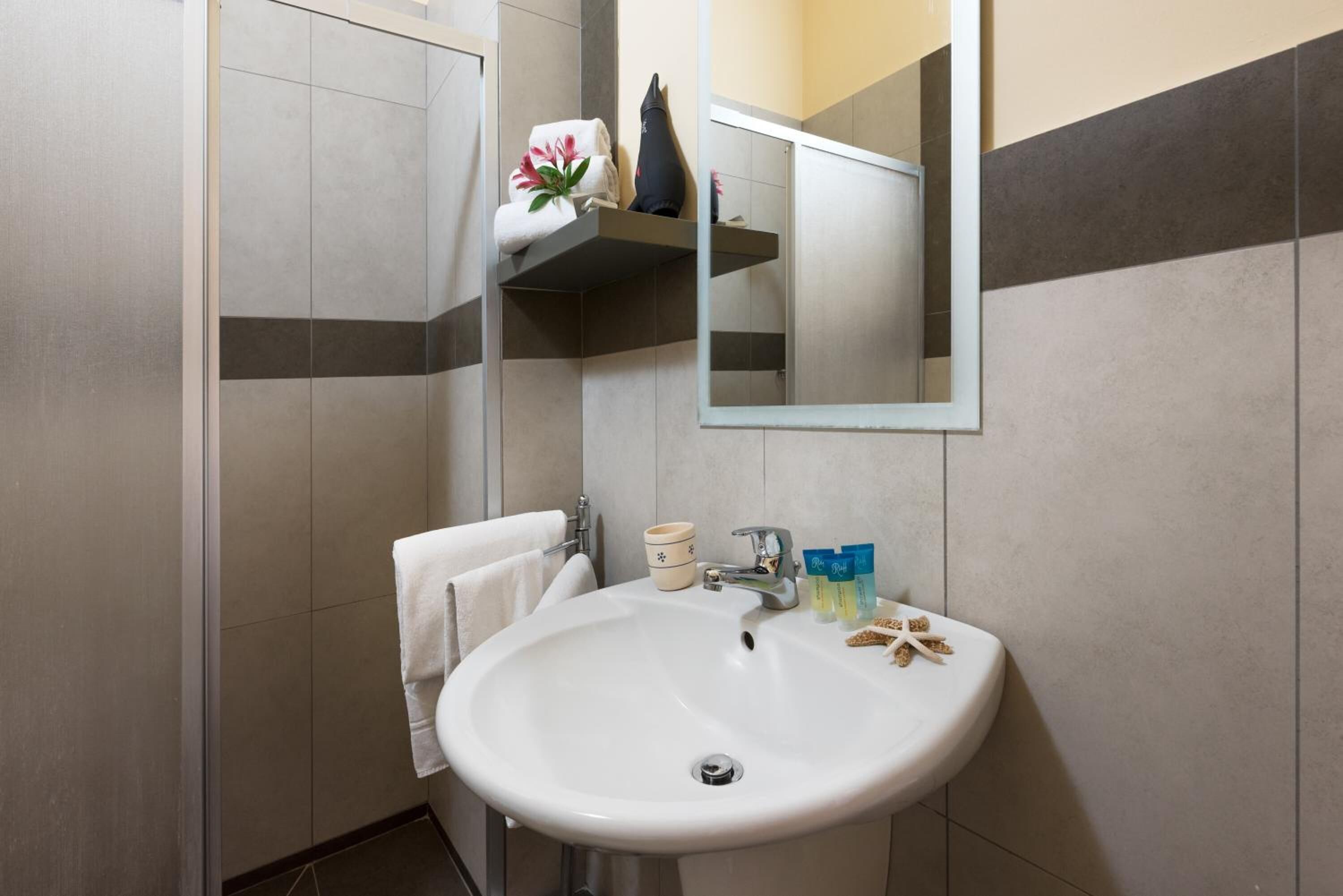 A bathroom with a white sink, a mirror, a towel rack, and a shelf with toiletries.