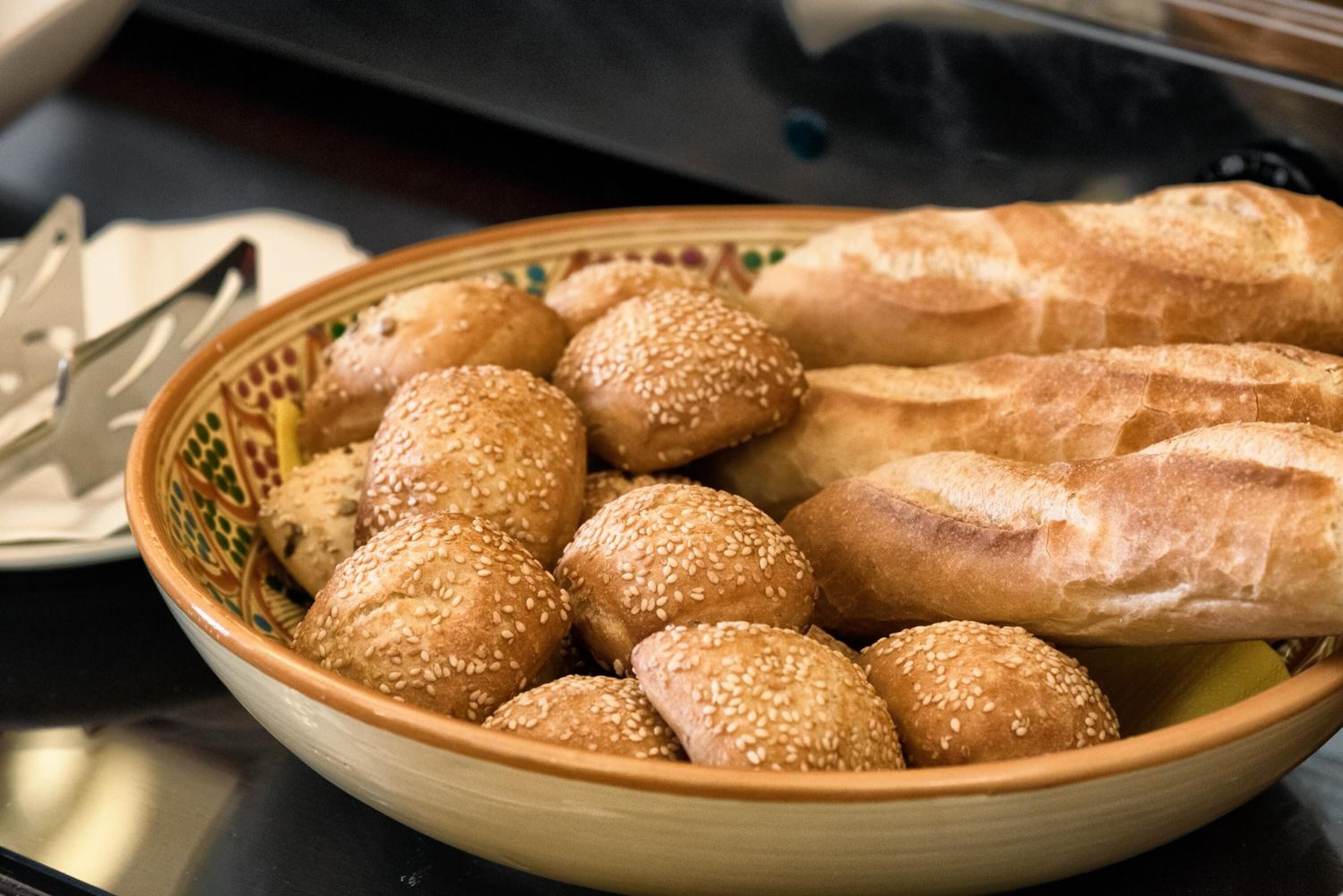 Un bol rempli de petits pains aux graines de sésame et des baguettes sur une table.
