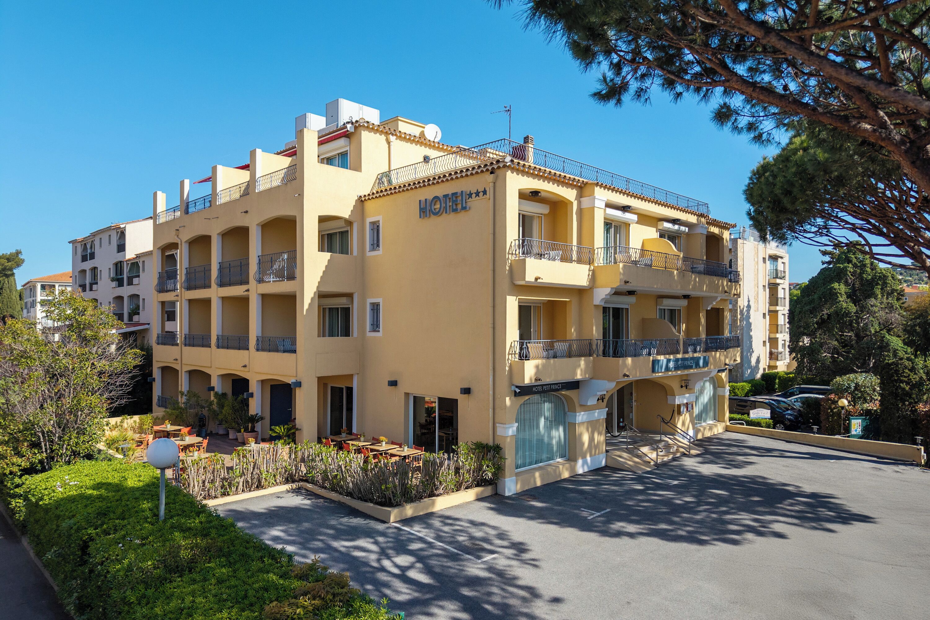A multi-story hotel with balconies, a parking area, and surrounding greenery.