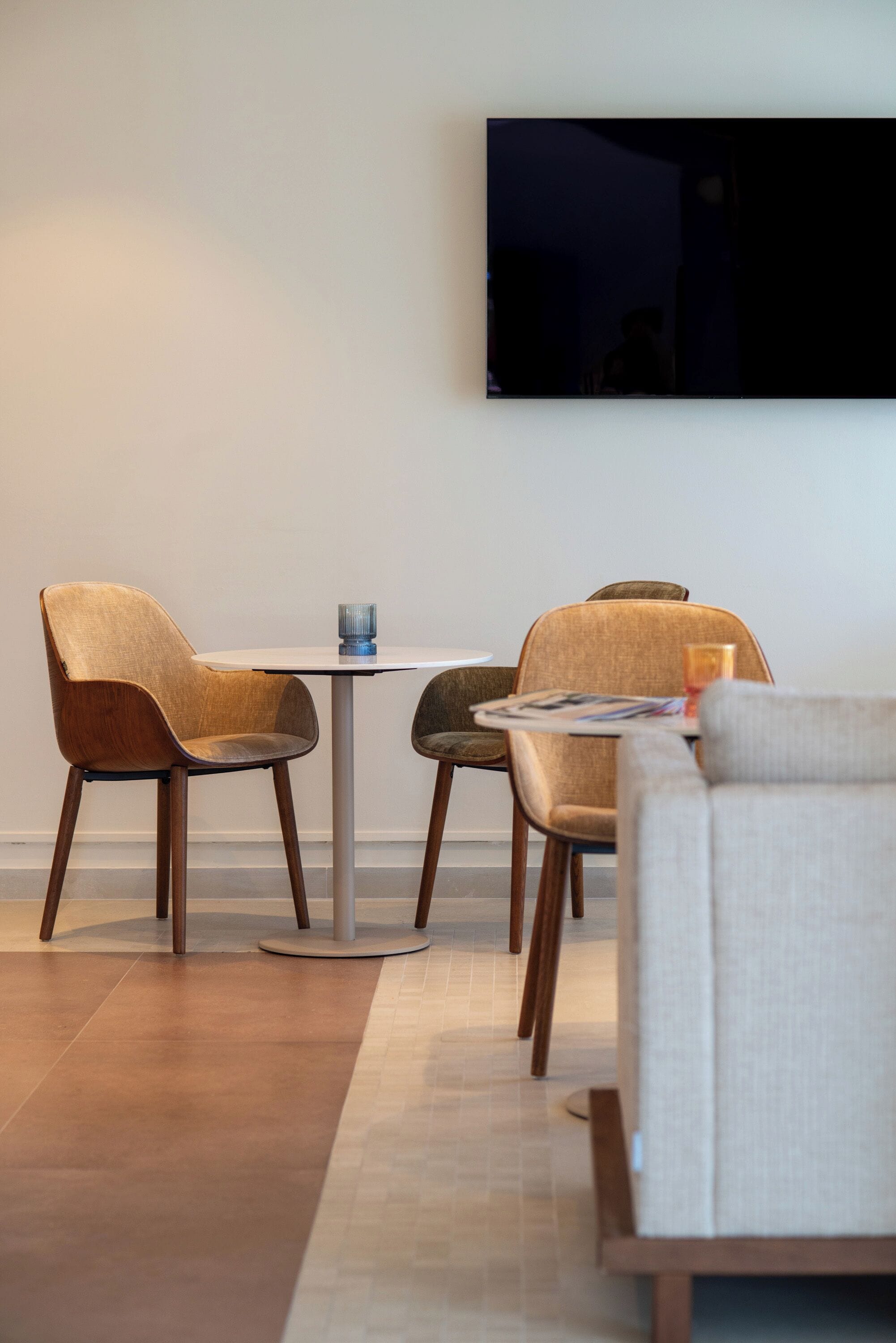Una sala de estar moderna con un televisor de pantalla plana montado en la pared, dos sillones, una mesa redonda de centro y un sofá.