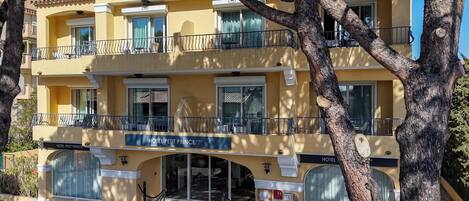 A two-story hotel with a yellow facade, balconies, and a sign reading 'HOTEL PETIT PRINCE'.