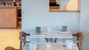 A dining area with a table set for two, a bust sculpture on the wall, and a kitchen in the background.