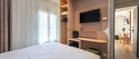 Una camera d'albergo con un letto grande, una scrivania con televisore a schermo piatto, una zona salotto e vista sul corridoio.