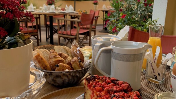 A table set with a red umbrella, a basket of croissants, a pie, and a knife. - Hotel Le Petit Prince (Sainte-Maxime)
