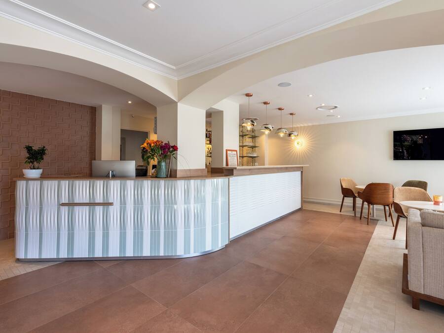 Una cocina moderna con una isla curva, un comedor con una mesa redonda y sillas, y una sala de estar con sofá y televisor de pantalla plana montado en la pared.