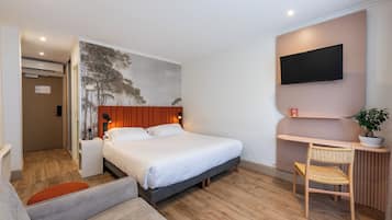 Habitación de hotel con cama, escritorio, silla, televisor y estante en la pared.