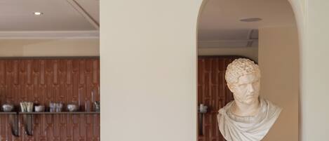 Una escultura de busto de mármol en un nicho dentro de una habitación con paneles de madera y una cocina moderna al fondo.