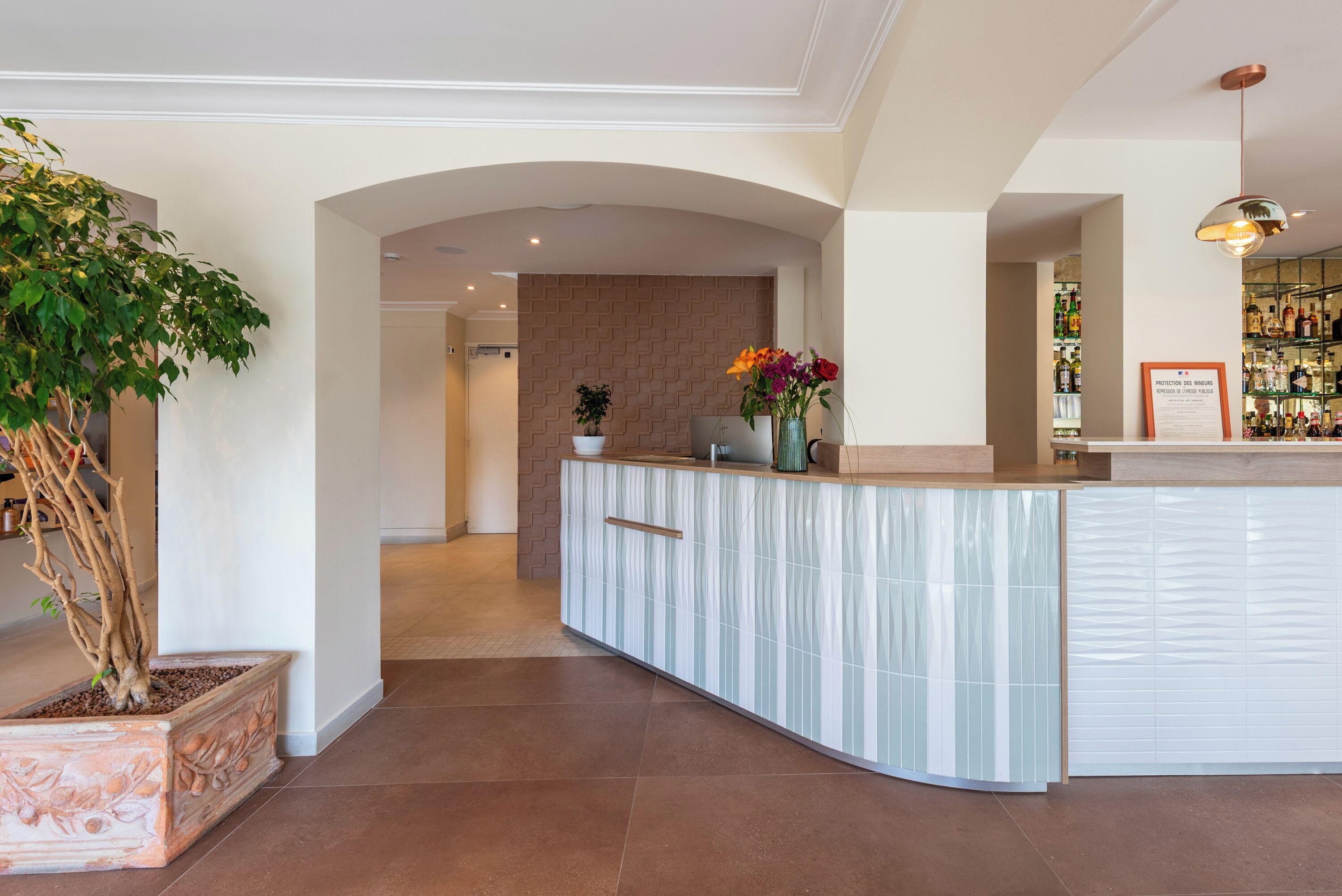 A modern reception area with a curved counter, a potted plant, and a wall-mounted sign.