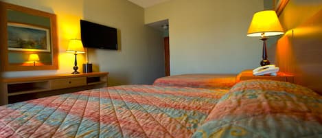 A hotel room with two beds, a flat-screen TV mounted on the wall, a wooden nightstand with a lamp, and a painting on the wall.