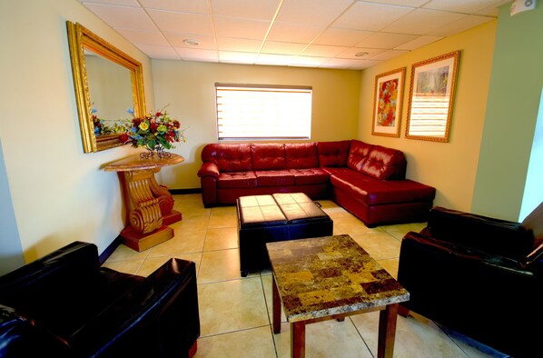 A living room with a red leather sofa, a wooden coffee table, and a large mirror on the wall. - Hotel Consulado Inn (Ciudad Juárez)