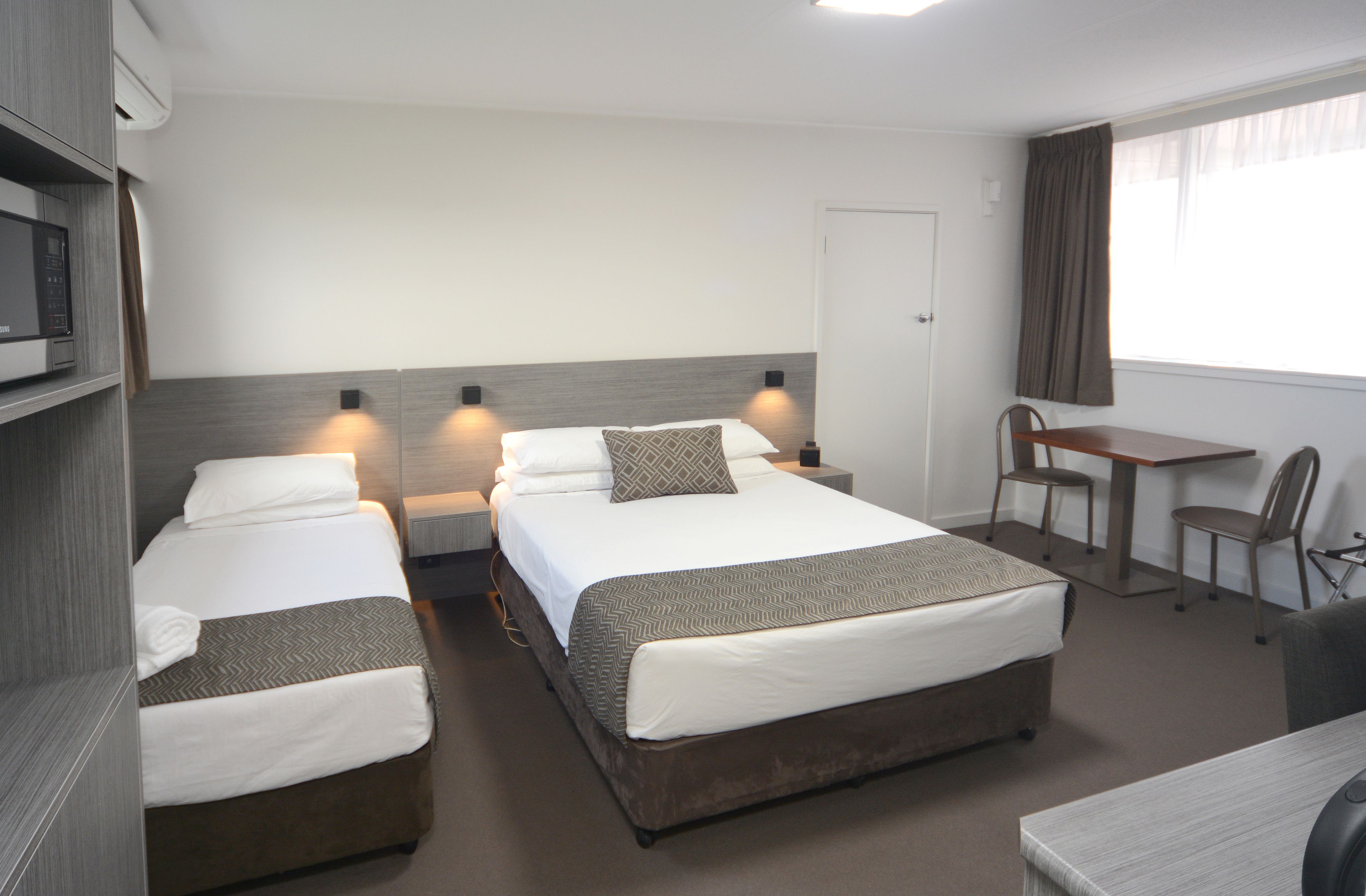 A hotel room with two beds, a desk, and a chair.