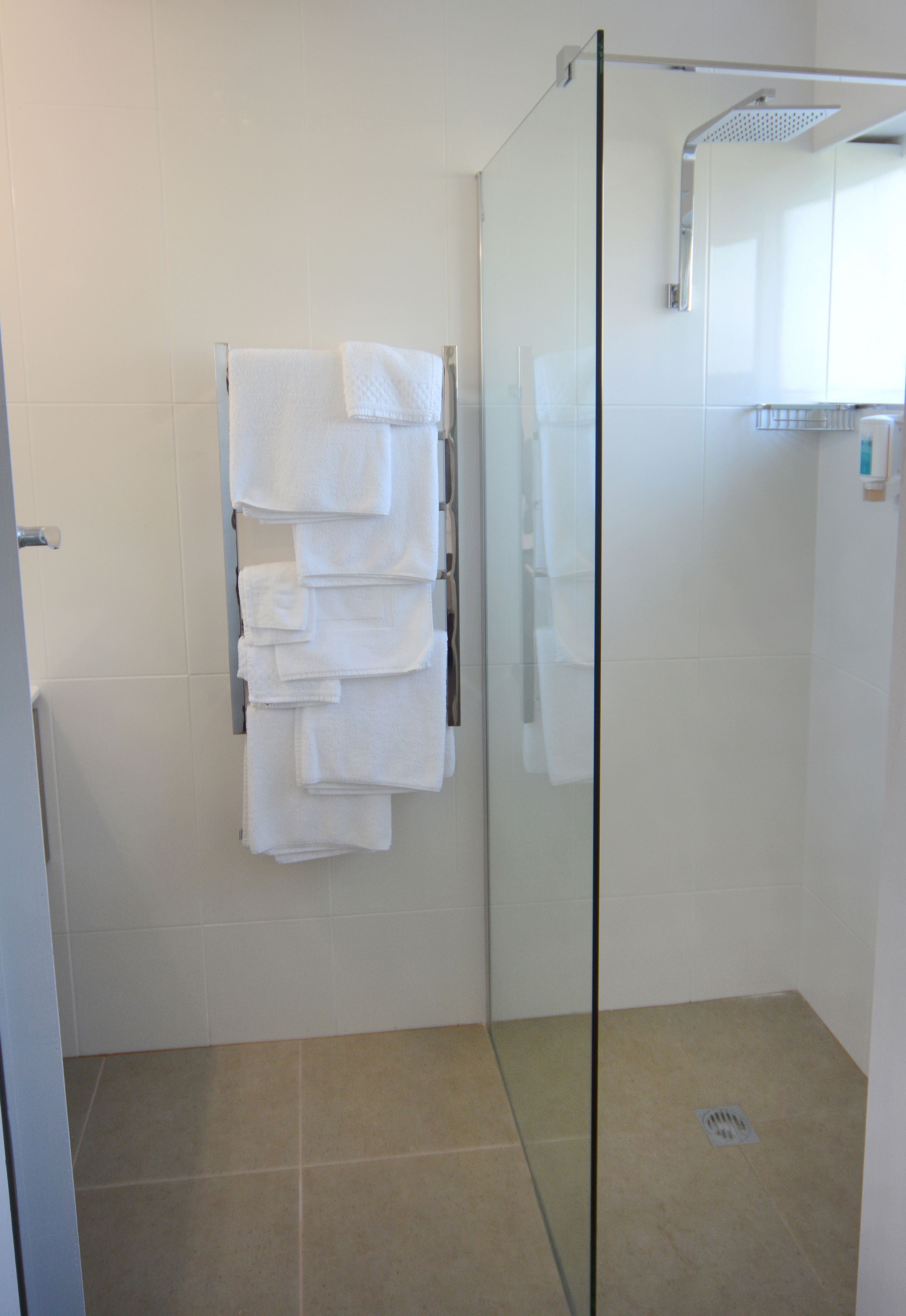 A glass-enclosed shower with a glass door, white tiled walls, and a towel rack with folded towels.