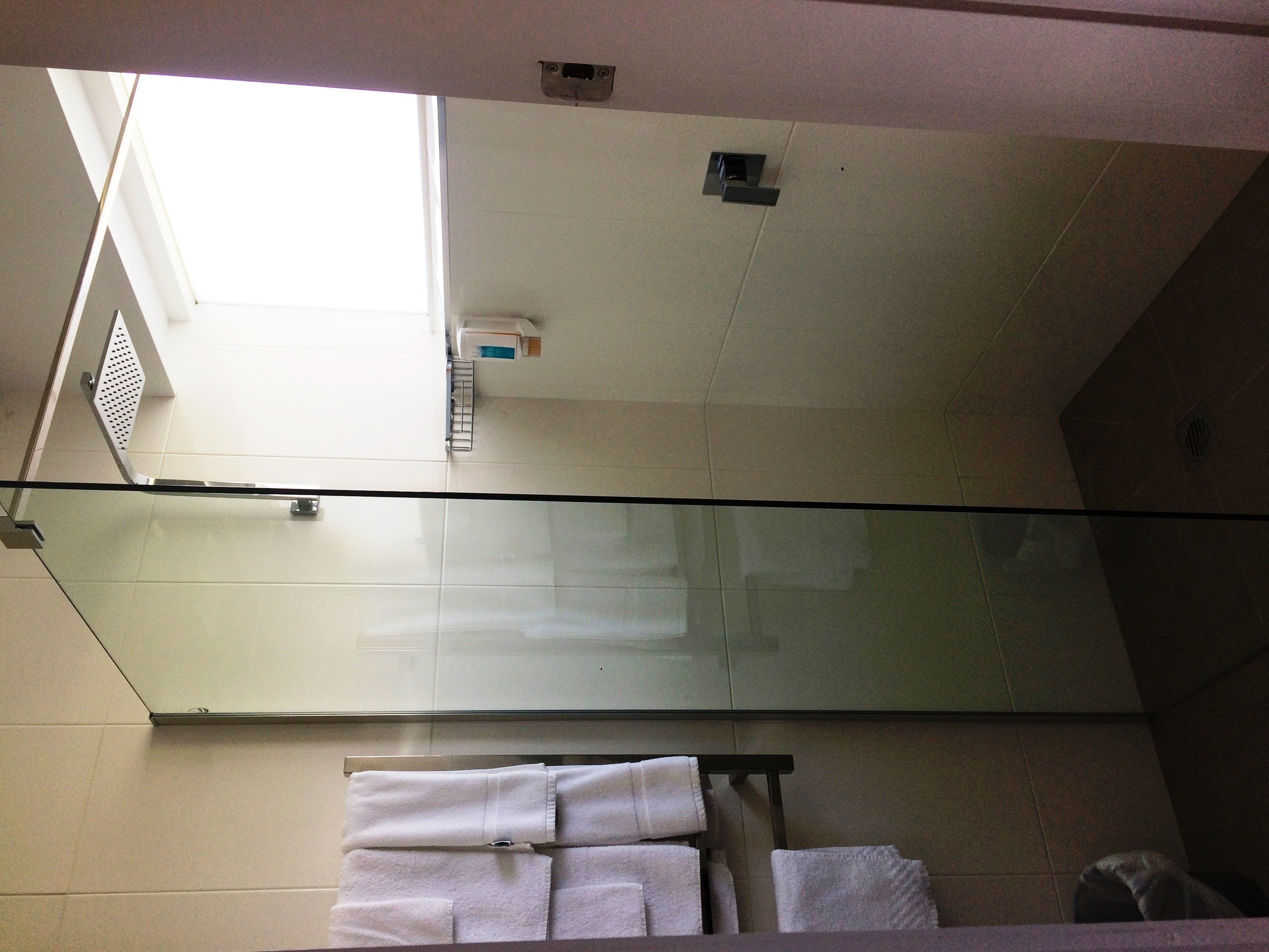 A bathroom with a glass partition, white towels, and a ceiling vent.