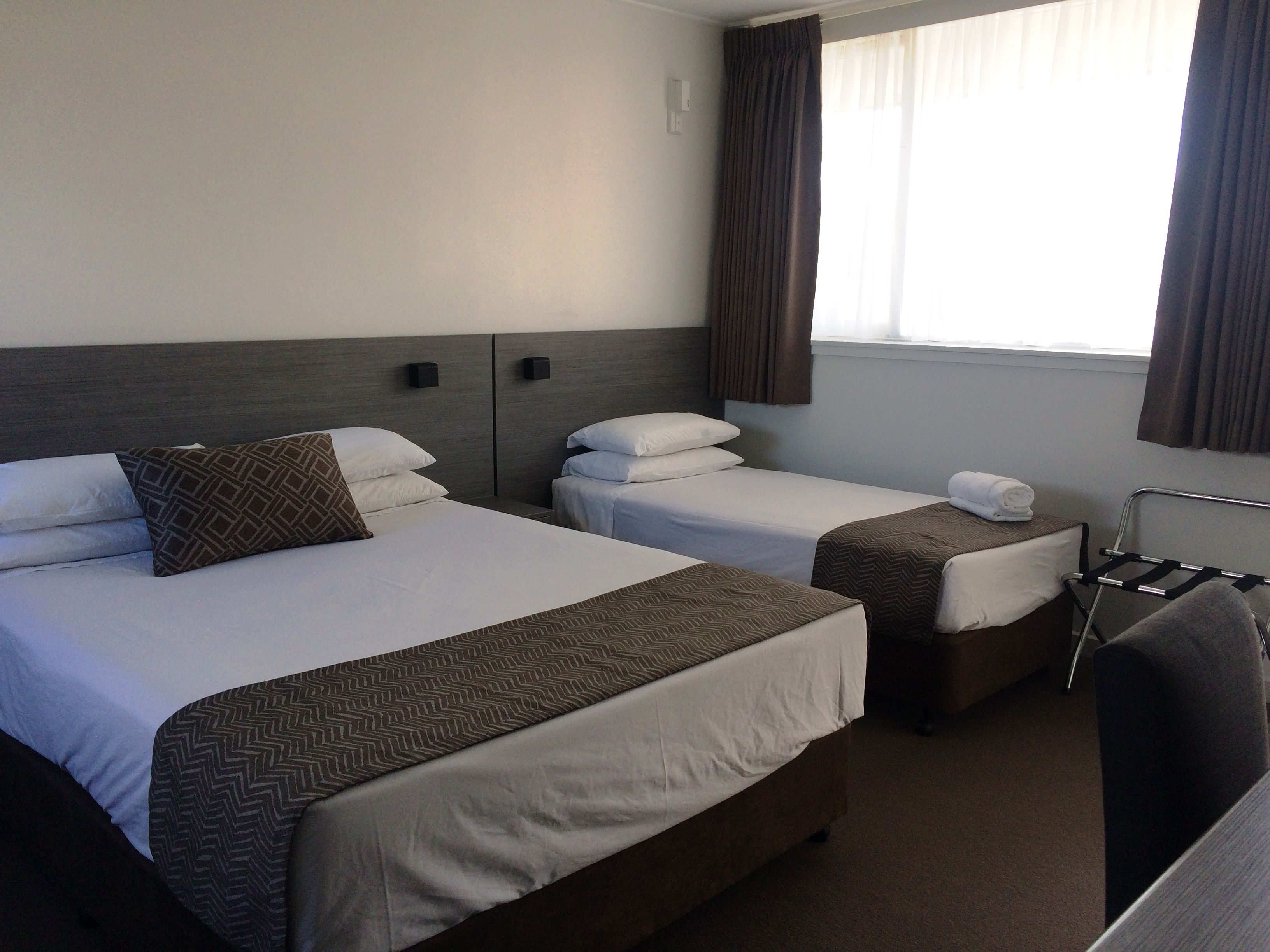 Ein Hotelzimmer mit zwei Betten, einem kleinen Tisch, einem Stuhl und einem Fenster mit Vorhängen.